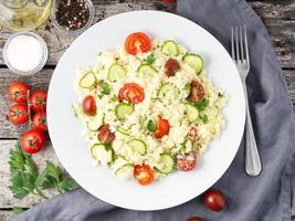 fresh diet vegetable salad with couscous, tomatoes, cucumbers, parsley, dark rustic wooden table, top view photo