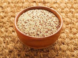 Raw Quinoa in wooden bowl, superfood. Brown sisal mat background, side view. photo