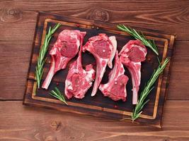 Raw lamb cutlets on bone on dark brown wooden background, lamb ribs, top view. photo