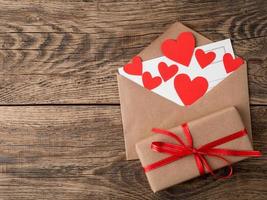 card and red hearts in open envelope from brown Kraft paper. Gift box with red ribbon on wooden aged vintage background. Greetings with Valentine's day with copy space for your text photo