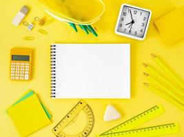 Top view of bright yellow office desktop with blank notepad, school supplies on table, space for text. Back to school concept. photo