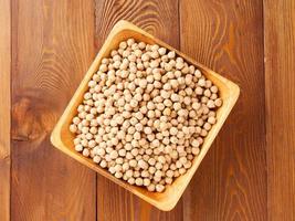 Dry raw chickpeas in wooden bowl on dark brown rustic background, top view photo