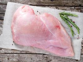 Raw whole big breast turkey fillet with fresh rosmary on a old rustic gray wooden background. photo