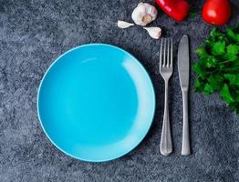 clean empty blue bright plate, fork and knife on gray concrete background, top view. photo