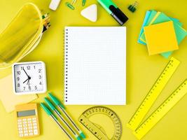 Top view of yellow office desktop with notebook in cage, school supplies on table, empty space for text. Back to school concept. photo