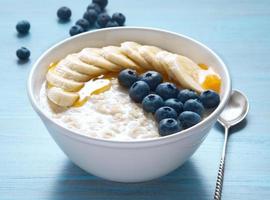 Oatmeal with bananas, blueberries, chia seeds, jam, honey on blue wooden background. Healthy breakfast. Side view. photo