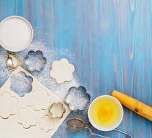 Raw puff pastry dough lies on a blue wooden table, sprinkled with flour. Figures for baking cut metal mold, sugar and egg in bowls photo