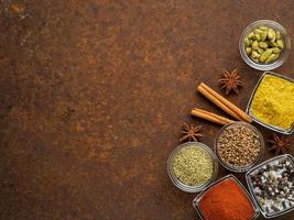 Set of various spices on a dark brown rusty metal table - coriander seeds, ground red pepper, salt, black pepper, rosemary, turmeric, curry, coriander, star anise, cinnamon. Top view, empty space. photo