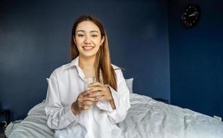 Young woman is lying on her bed smiling while holding a glass of milk, Healthy refreshment photo