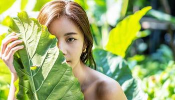 Portrait of a Beautiful asian young woman with natural makeup holds a big green leaf on a blurred green background. Spa and wellness. Youth, teens and skin care concept