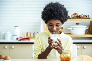 Child having breakfast. Happy cute African-American boy drinking milk and eating bread with egg. Kids eat on sunny morning. Healthy balanced nutrition for young kids. photo