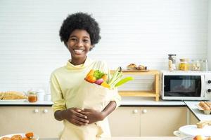 Happy healthy kid in the kitchen, Adorable Little boy smiling and holding paper bag with fresh food full of vegetables photo