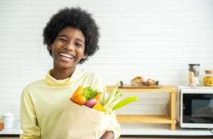 Happy healthy kid in the kitchen, Adorable Little boy smiling and holding paper bag with fresh food full of vegetables photo