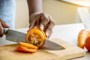 Primer plano de la mano de una chica afroamericana cortando tomates en una tabla de cortar con un cuchillo en la cocina foto