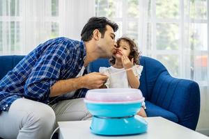 Caucasian family young father kissing his little daughter at mouth after eat cotton candy together on sofa at new house