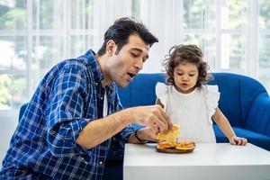 joven padre atractivo y pequeña hija linda disfrutando de pizza en un cómodo sofá de la sala de estar foto