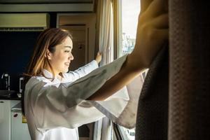 una joven y bella mujer encantada de pie junto al dormitorio y abriendo las cortinas, mira a la distancia de la ventana y recibe la bienvenida al nuevo día. las mujeres sonrientes se sienten emocionadas por las oportunidades o perspectivas de carrera en la vida. foto