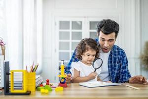 Little girl doing science experiments in the laboratory with father who looks through magnifying glass. Dad and daughter study biology and chemistry lessons with microscope. Homeschooling photo