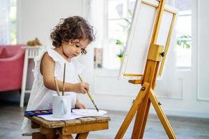 una pequeña artista linda usa un pincel de pintura acrílica para hacer sus dibujos sobre lienzo foto