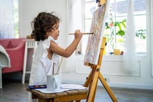 una pequeña y linda artista pintando un cuadro sobre lienzo con pinturas de acuarela en casa foto