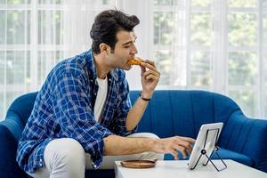 Man at home eating a slice of pizza food online together with her girlfriend in video conference with digital tablet for a online meeting in video call for social distancing
