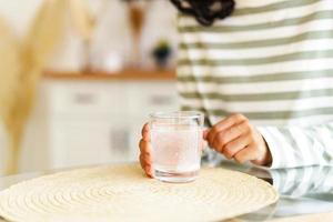 disolución de drogas efervescentes en un vaso de agua. mujer irreconocible tomando medicamentos en casa foto