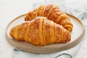 Two delicious croissants on plate and hot drink in mug. Morning French breakfast photo