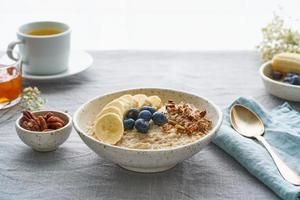 Whole oatmeal, large bowl of porridge with banana, blueberries, nuts for breakfast, photo