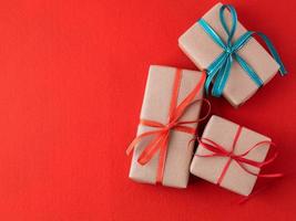 Background for Valentine's Day, birthday, holiday, shopping. Gifts from the store in a pack of Kraft brown paper with red ribbons on a bright red background photo