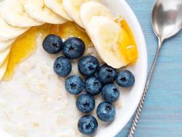 Oatmeal with bananas, blueberries, chia, jam, honey on blue wooden background. Healthy breakfast. Top view, close-up photo