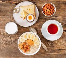 Breakfast in the morning, on a wooden table, top view. A glass of milk, tea, oatmeal with fruits and nuts, soft-boiled egg. photo