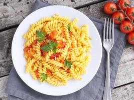 Pasta fusilli with tomatoes with parsley on a old rustic gray wooden background, photo