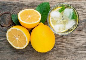 Lemonade in a glass, a lemon half, fresh leaves on old wooden table. A refreshing cold drink of water with ice, mint and slices of lemon, top view photo
