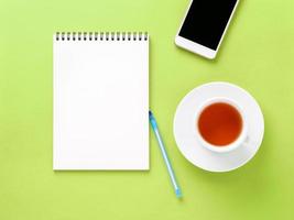 Top view of modern bright green office desktop with blank notepad, cup of tea, smartphone. Mock up, empty space photo