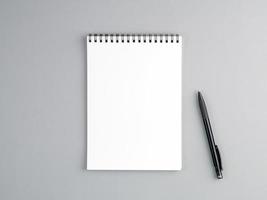 blank sheet of notebook with a spiral and pen on a neutral gray textured background photo