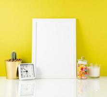 Blank white frame, clock, succulent, candy on a white table against the yellow wall. Mockup with copy space. photo