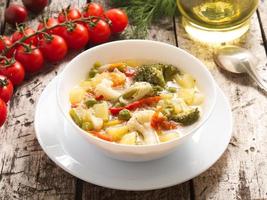 Minestrone vegetable soup with tomato, celery, carrot, zucchini, broccoli. Side view, gray rustic wooden table photo