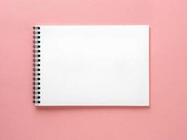 Blank notepad white page on pink desk, color background. Top view, flat lay. photo