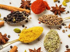 Mix of Indian spices in spoons on white wooden table, side view, selective focus, macro. Seasonings - rosemary, curry, pepper, paprika. photo