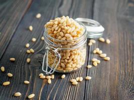 Side view of glass jar with a handful of pine nut, cedar nuts on a wooden background, selective focus photo