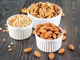 assorted nuts in white bowl on wooden dark background, mix of walnuts, almonds and cedar, side view