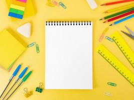 Top view of modern bright yellow office desktop with blank notepad, school supplies on table. Back to school concept. photo