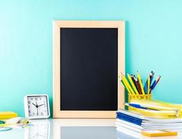 Chalkboard and school supplies on white table by the blue wall. Side view, empty space. Back to school concept.