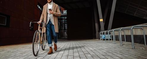 foto de portada. hipster caminando con bicicleta y usando un teléfono inteligente. yendo del trabajo.