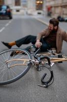 accidente de bicicleta en la ciudad. hombre ciclista se cayó de la bicicleta de carretera mientras andaba en bicicleta. lesión en bicicleta, rodilla lesionada foto