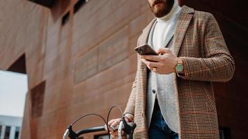 detalle de la sección media de la mano con el teléfono. hombre de negocios con teléfono móvil. en el camino al trabajo con bicicleta foto