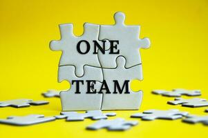 One team text on jigsaw puzzle with yellow background. Teamwork concept photo