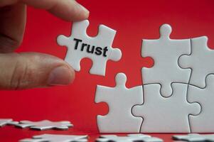 Trust text on jigsaw puzzle with red background - Working relationship and trust concept photo