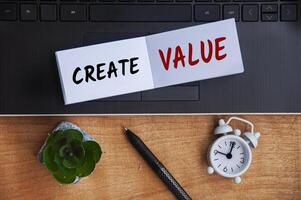 Create value text on notepad with laptop, clock, pen and wooden background. Business concept photo