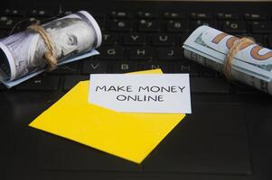 Make money online text on notepad in an envelope with laptop and bank notes background. photo